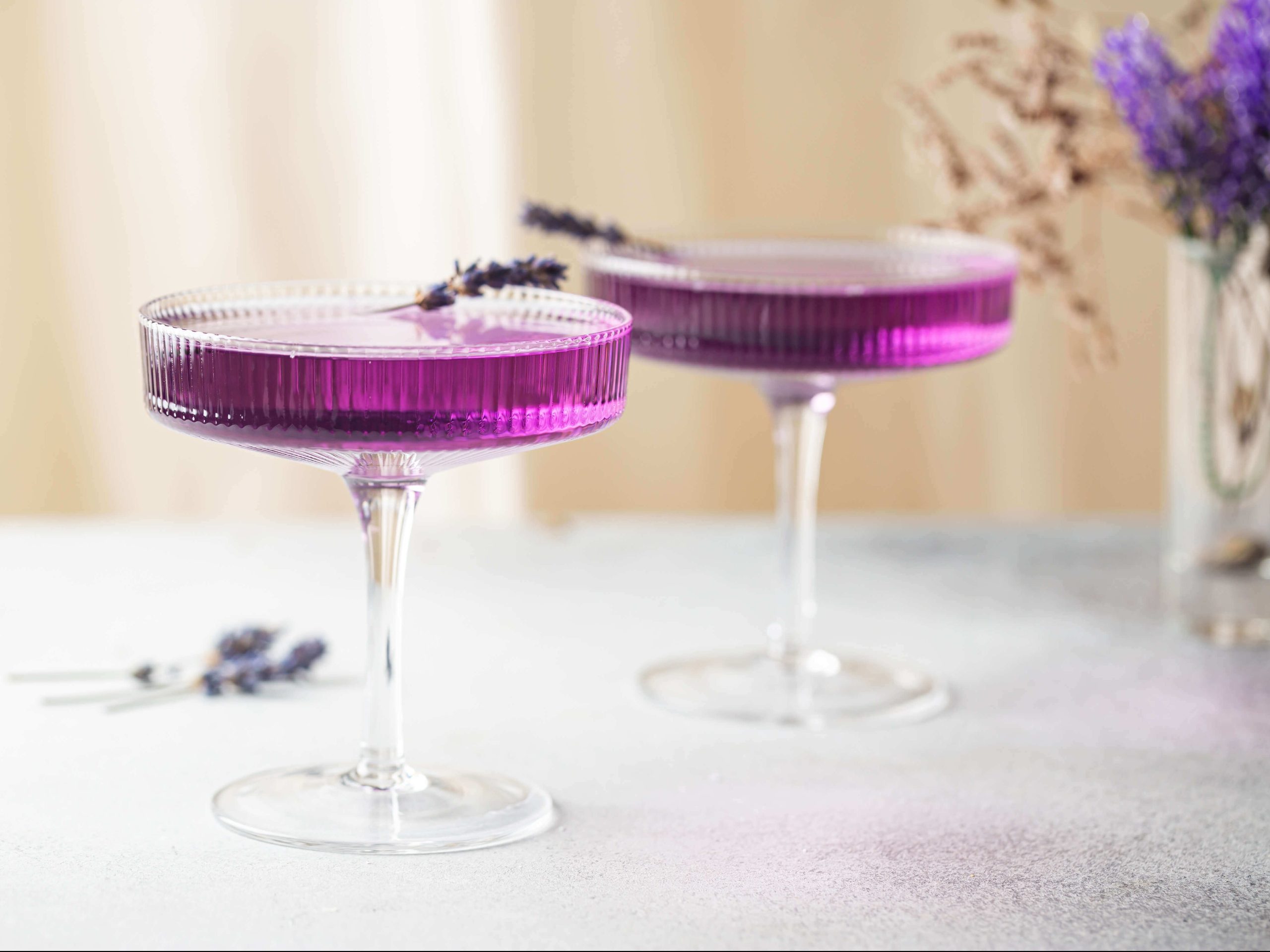 Two lavender cocktails in coupe glasses and garnished with lavender sprigs