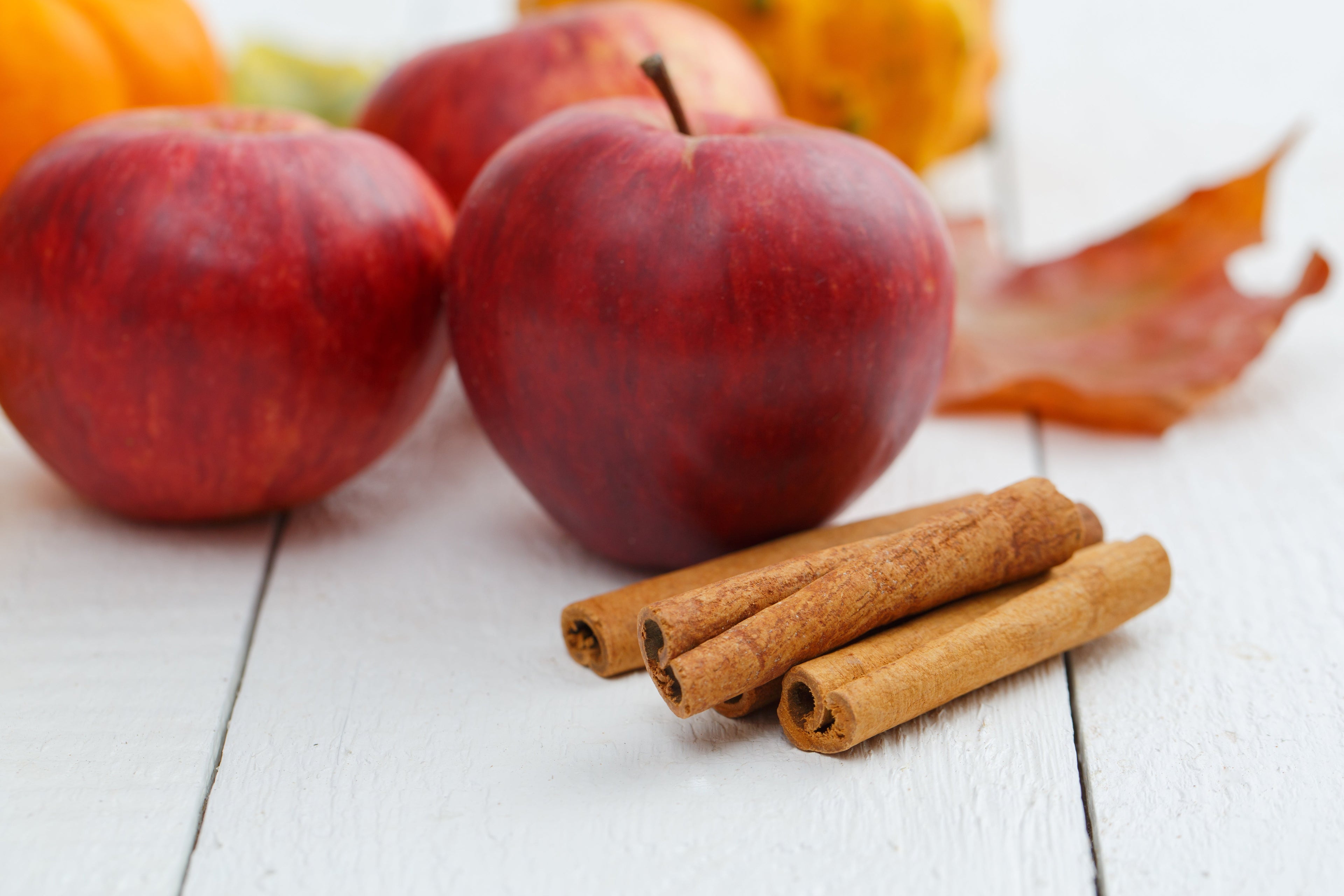 Red apples, cinnamon sticks and fall leaves on a white wooden table.