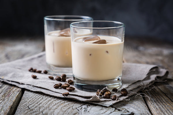 Two iced coffee drinks on top of a grey napkin sprinkled with coffee beans.