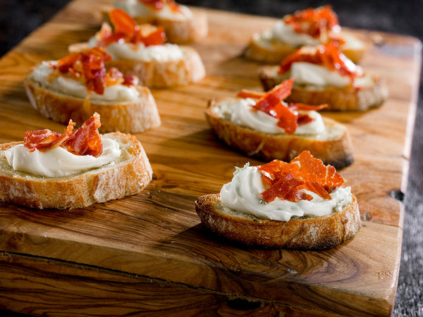 Crostini's on a wooden serving board topped with prosciutto.