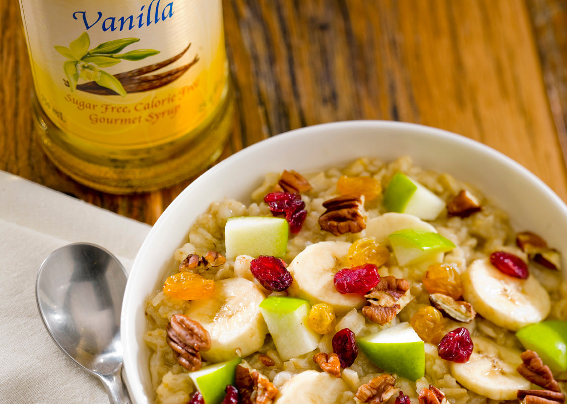 Bowl of oatmeal with walnuts, apples and dried cranberries next to a Monin Sugar Free Vanilla Syrup.