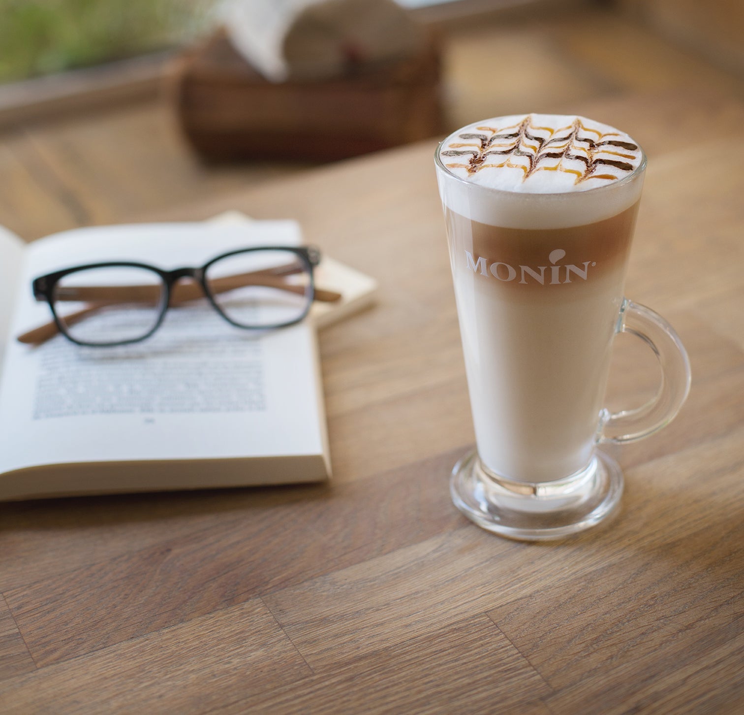 Cafe Latte in a tall Monin glass with chocolate and caramel drizzle on top of foam.