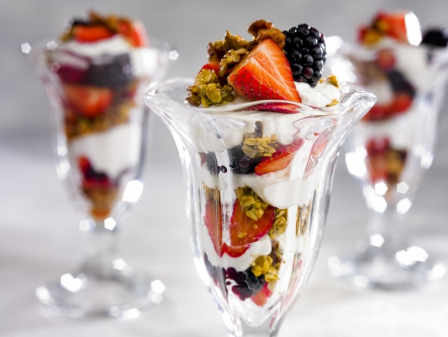 Three yogurt parfaits in a tall glass each with fresh fruit and granola.