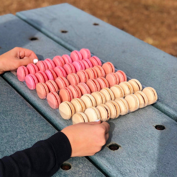 A person holding a tray of macarons colored in three different shades of pink.