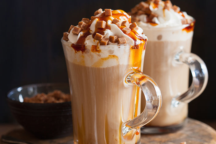 Two Toffee Mocha Lattes in a tall glass topped with whipped cream, caramel bits, and caramel sauce.