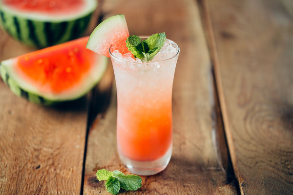 Watermelon cocktail in tall glass garnished with a watermelon slice and mint leaves.