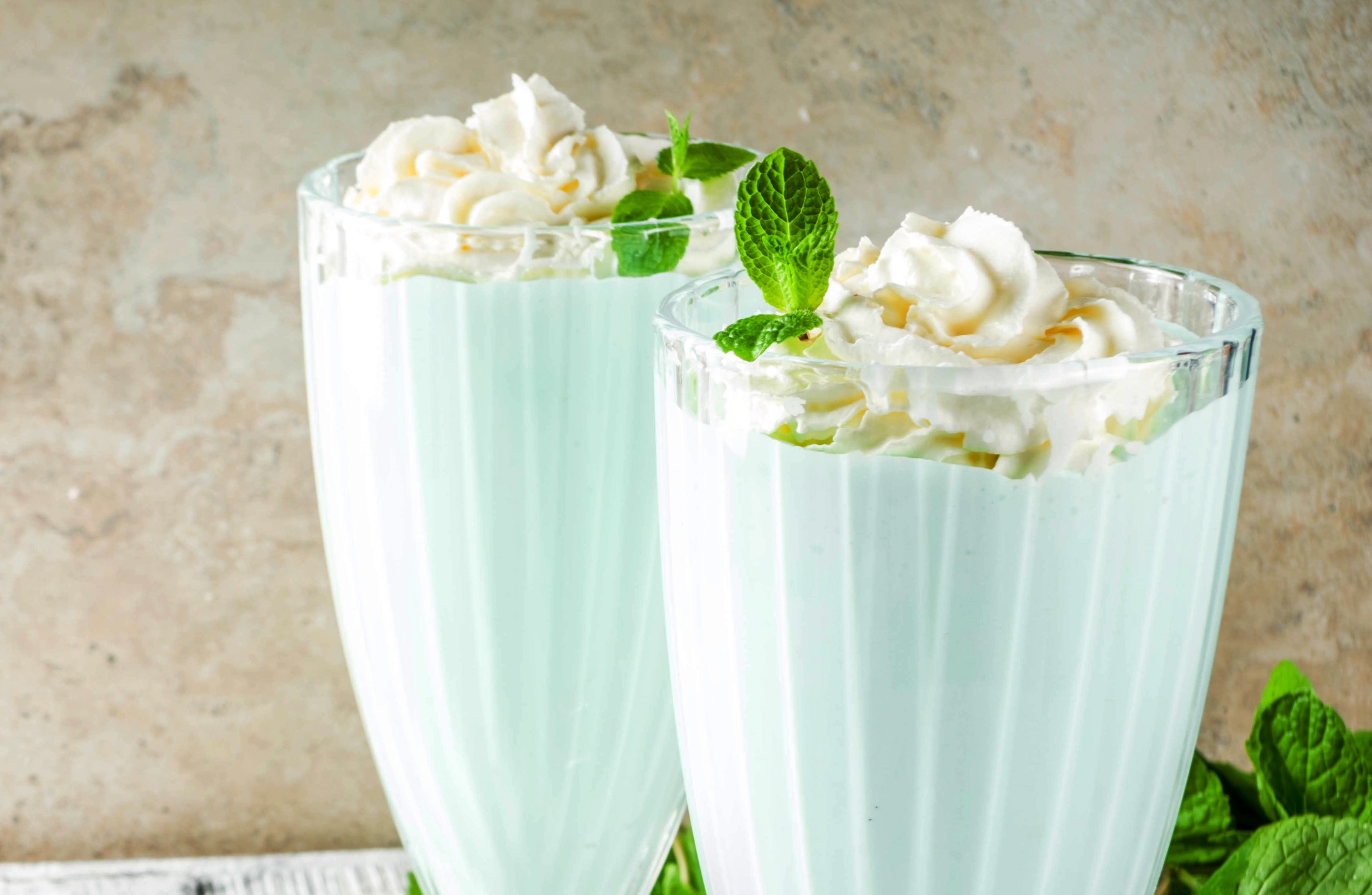 Summer refreshing cocktail, shamrock mint shake, sweet milk drink with fresh mint leaves, wooden background copy space